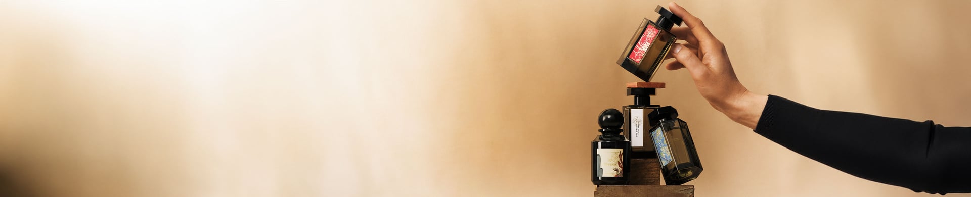 Right arm holding up four fragrance bottles balanced on wooden blocks on a beige background.jpg